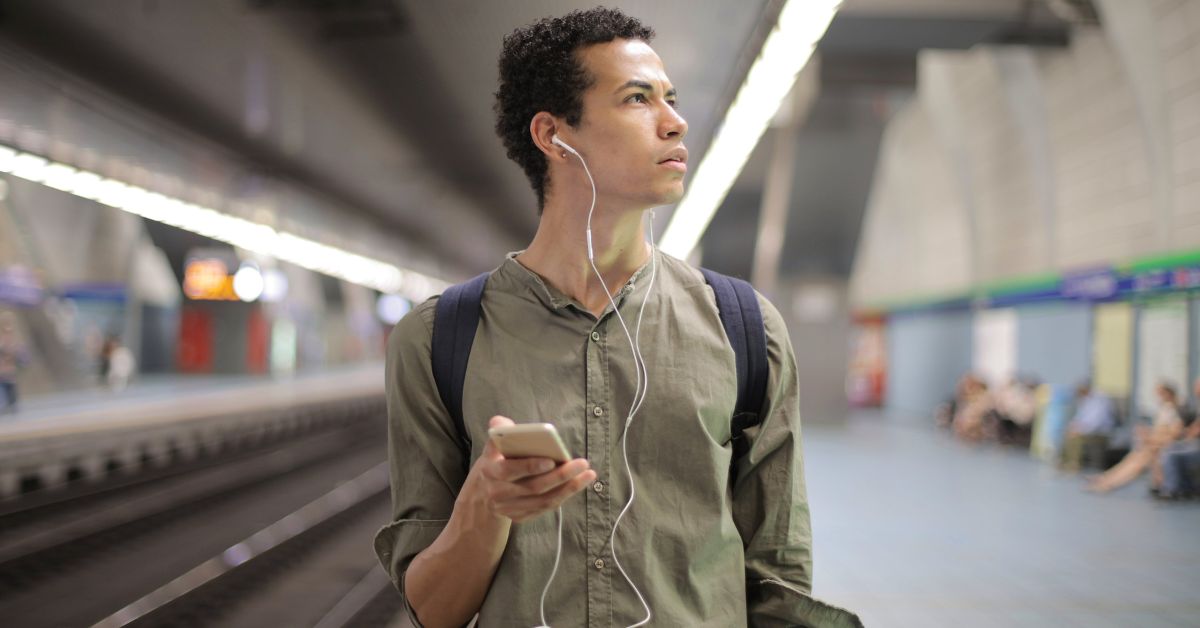 Man standing in a metro station with a mobile phone and wired earbuds