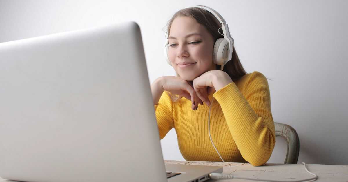 Woman in sweater and headphones sitting in front a laptop and smiling